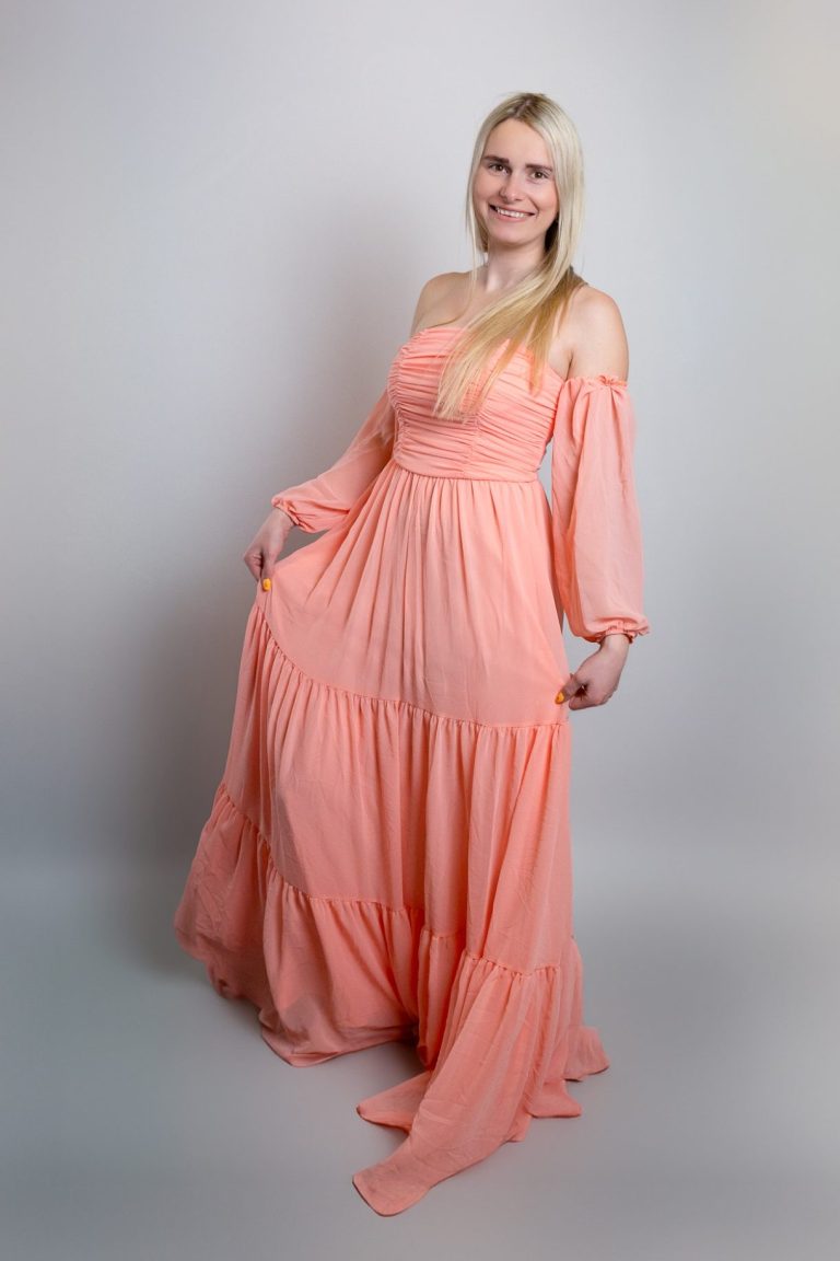 Frau in einem langen, hellkorallenfarbenen Kleid mit langen Ärmeln und langen Haaren.