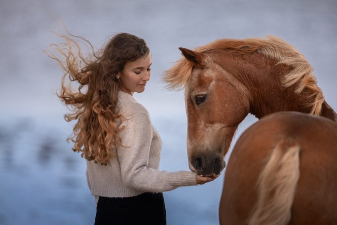 Junge Frau mit langen Locken, die sanft ein Pferd streichelt.