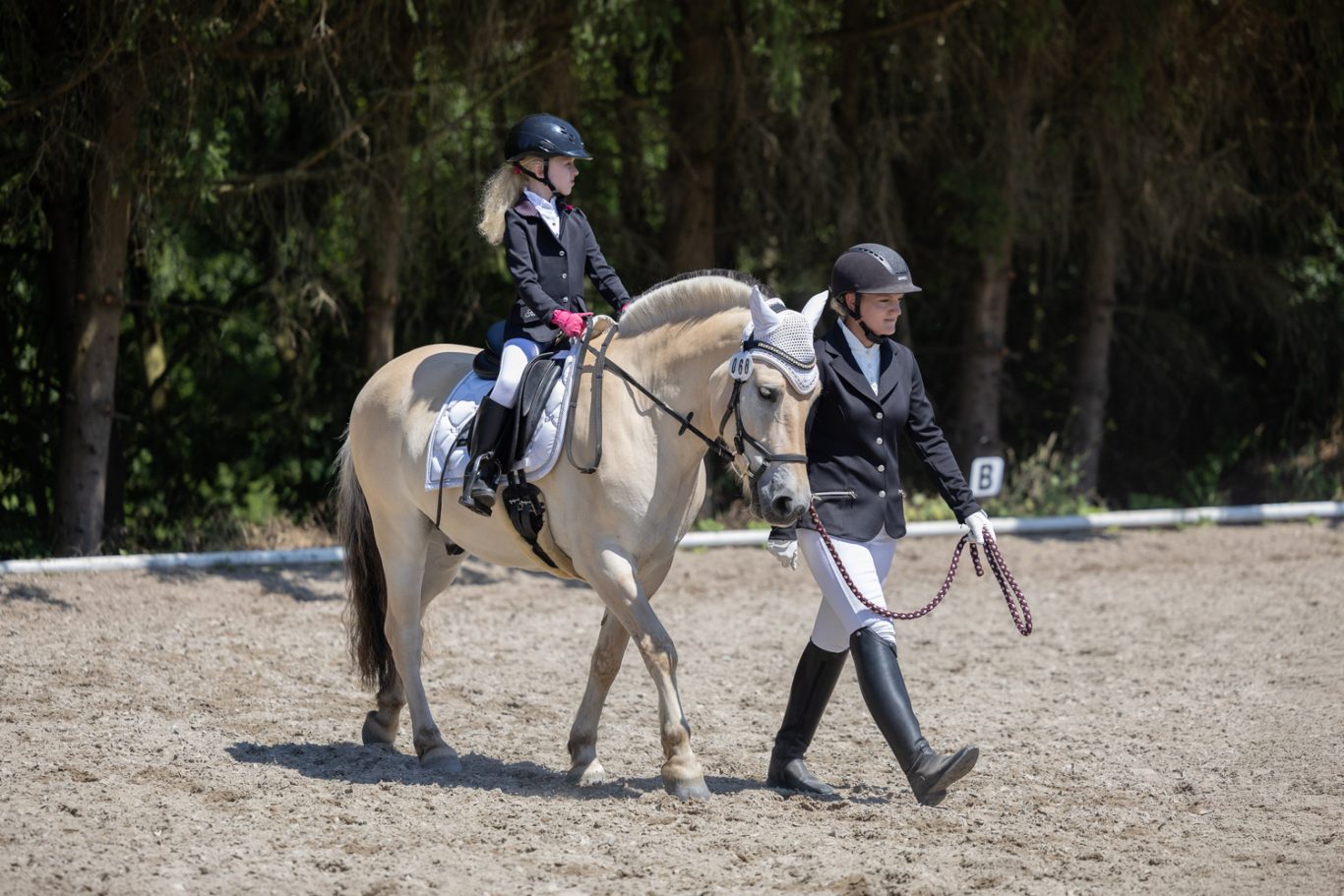 Ein Kind reitet auf einem hellen Pferd, während eine erwachsene Begleitperson führt.
