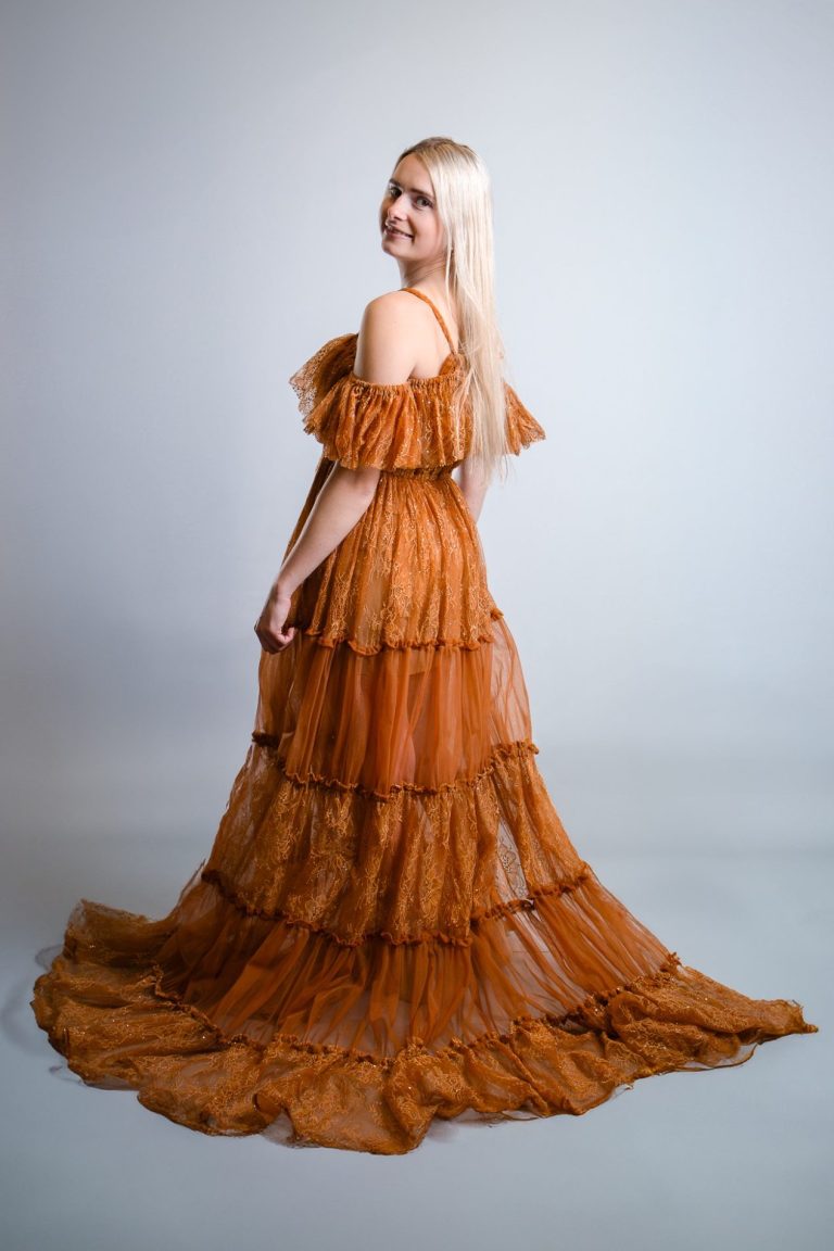 Frau mit langen, blonden Haaren trägt ein elegantes, schulterfreies, schichtetes Kleid.