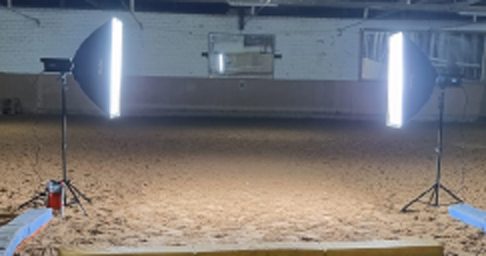 Beleuchteter Bereich mit zwei Scheinwerfern vor einem Sandboden.