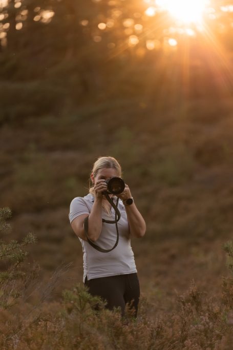 Frau mit Kamera fotografiert im Sonnenuntergang auf einer Wiese.