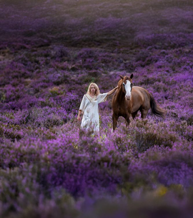 Eine Frau in einem weißen Kleid mit Pferd in der Heide
