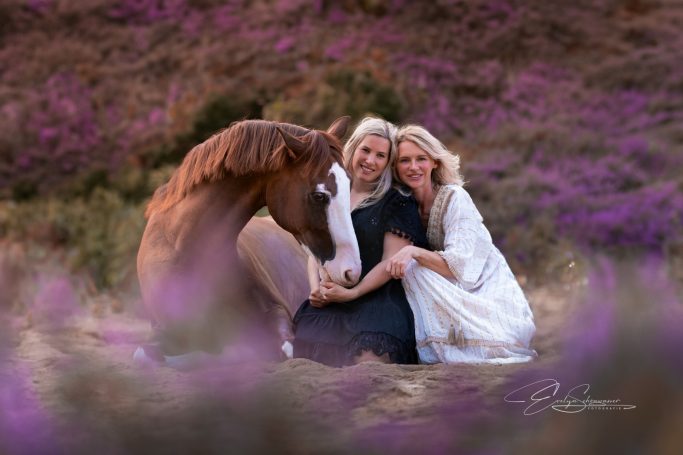 Zwei Frauen sitzen mit einem Pferd in einer blühenden Landschaft.