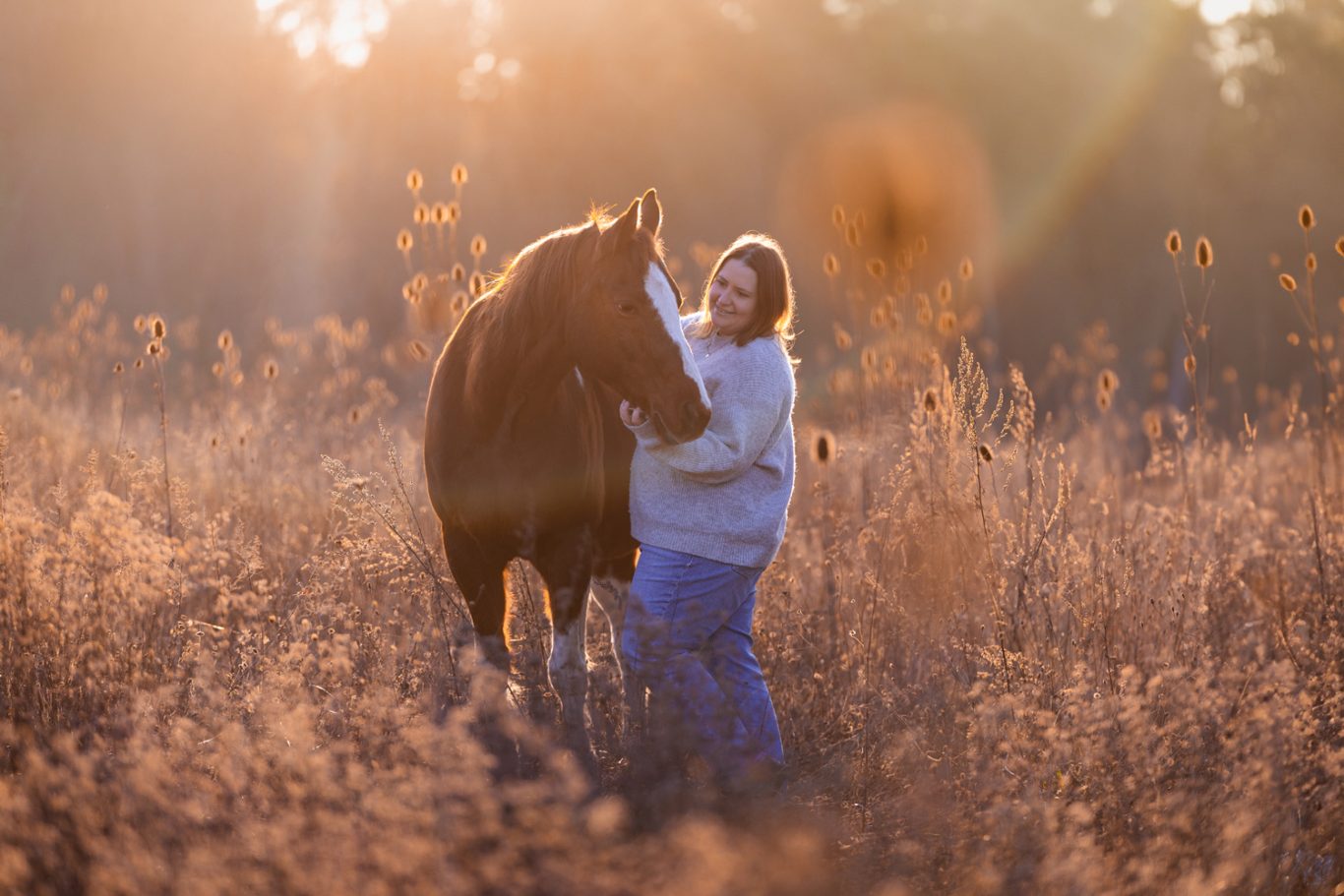 Frau umarmt ein Pferd in einem sonnigen Feld mit hohen Gräsern.