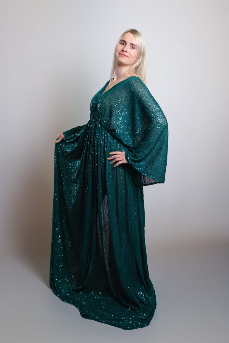 Eine Frau in einem eleganten, glitzernden, türkisfarbenen Kleid mit weiten Ärmeln.